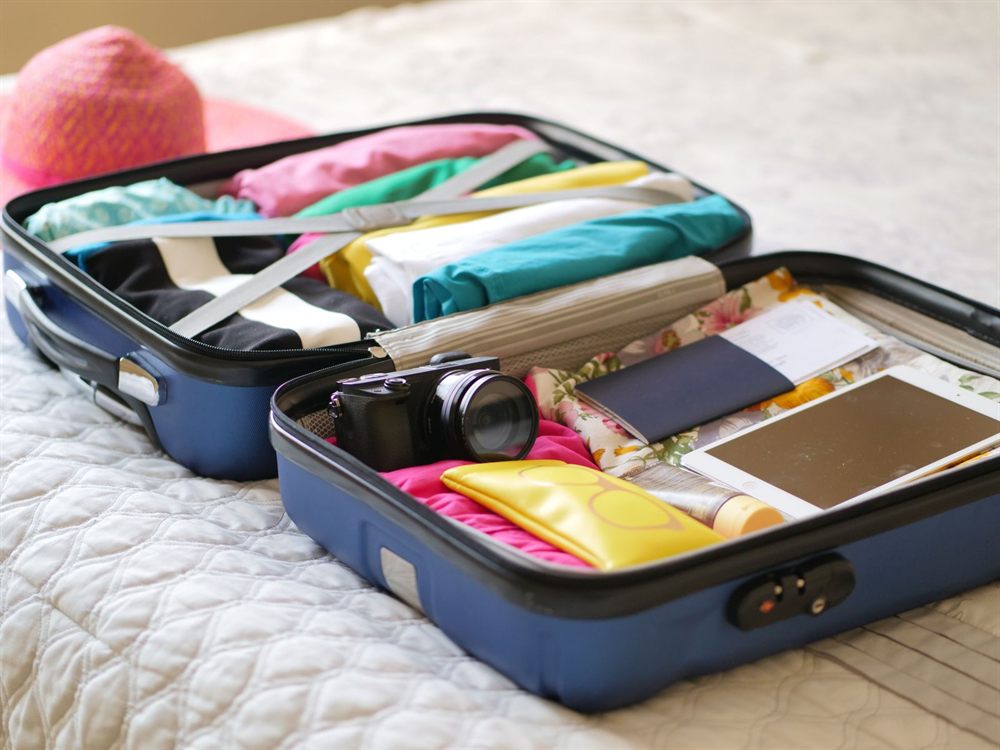 Open suitcase with a passport, camera and summer clothes ready for travel